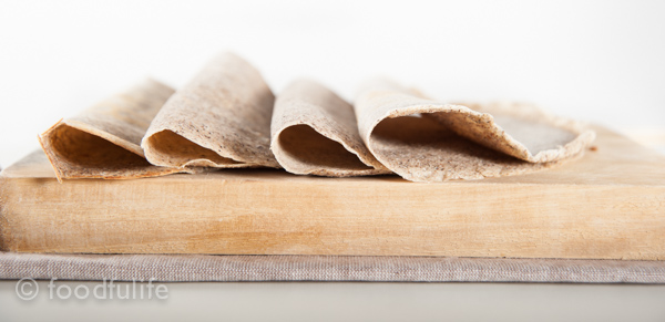 crepes on rectangular cutting board on a beige cutting mat, with white background