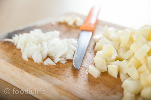 Onions and potatoes on cutting board with knife.