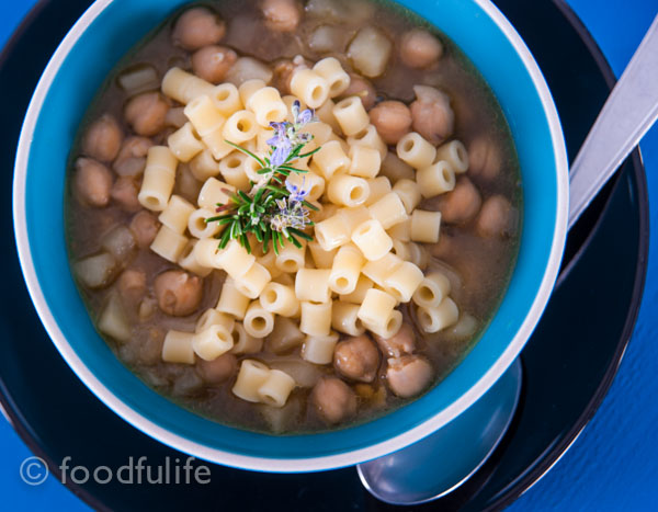 Chickpea and potato soup with rosemary in a blue bowl on a black dish, on blue painted wood board. Zuppa di ceci e patate al rosmarino.